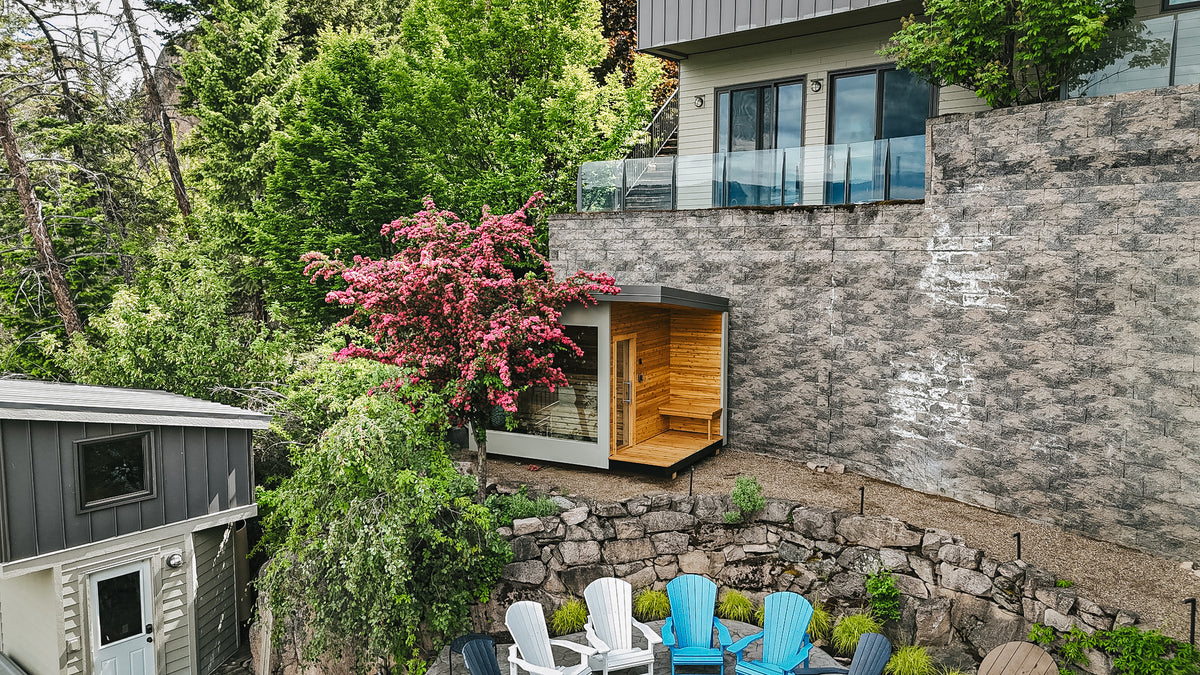 Aerial view of a modular cedar sauna set against a stone retaining wall on a lakefront terrace