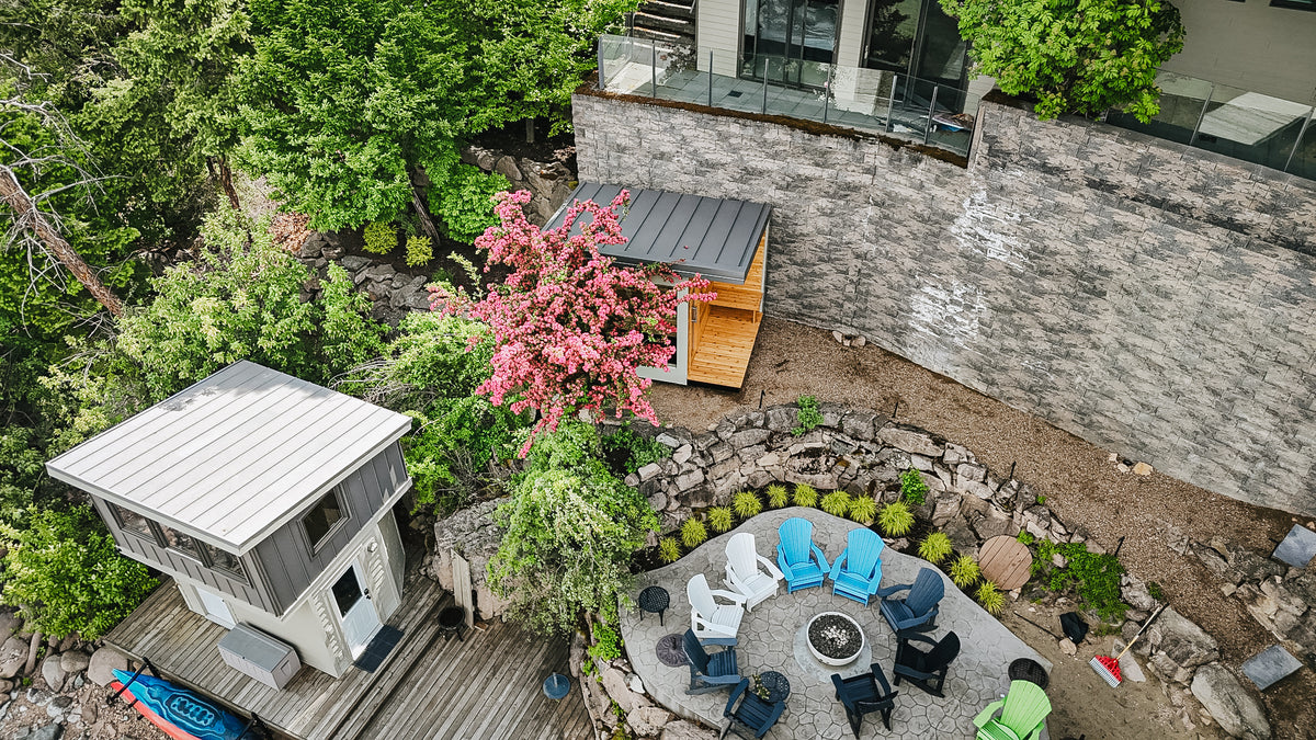 Top-down drone view of a fire pit patio, guest cabin, and Elk Ridge Modular sauna on a waterfront property