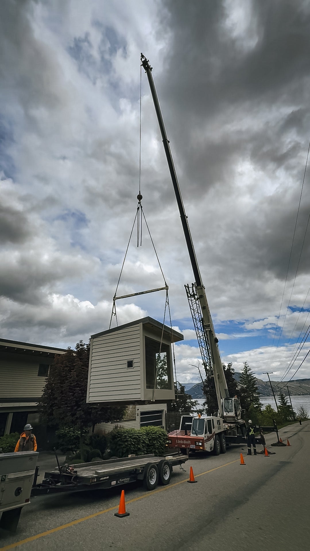 Modular sauna suspended from a crane above the street, lake behind
