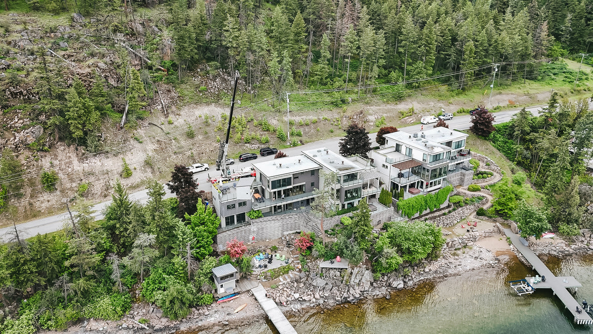 Aerial showing a crane reaching from the road over a house to the waterfront terrace below