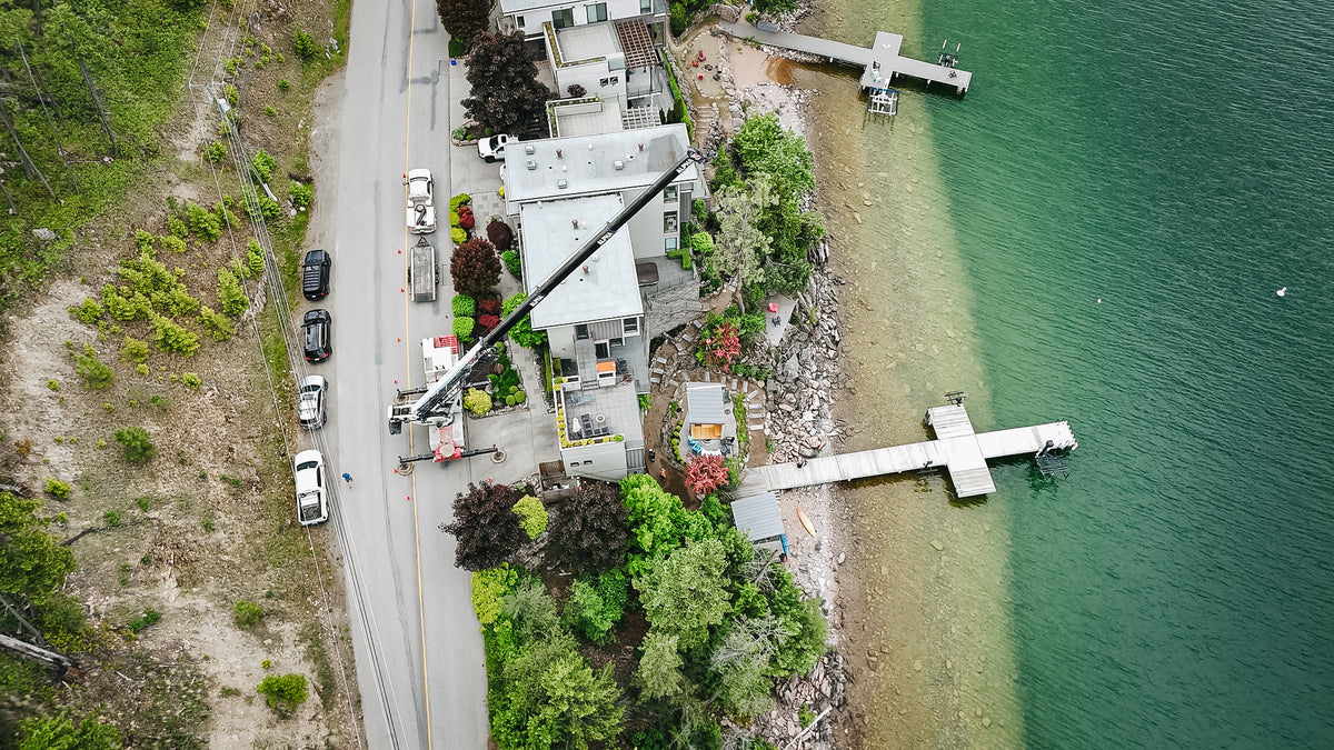 Top-down drone view of a crane boom spanning a house during a sauna installation