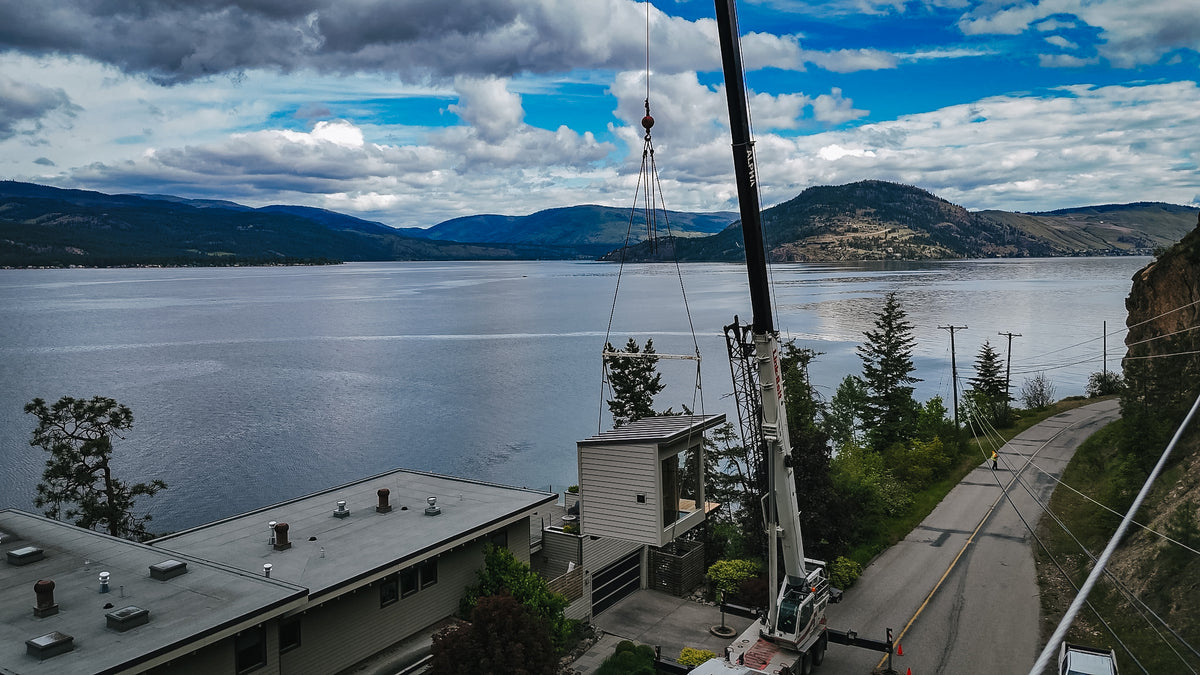 Modular sauna high on the crane hook beside the boom with Okanagan Lake behind
