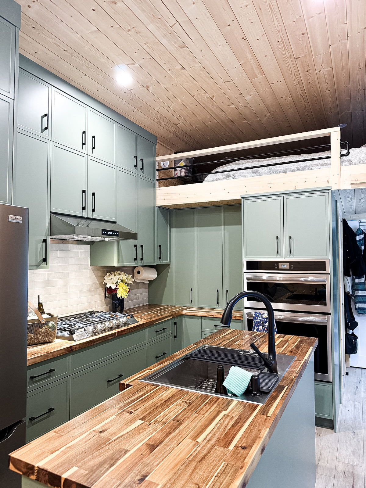 Olive green slim shaker kitchen with butcher block island and sleeping loft above in a Modern Cabin