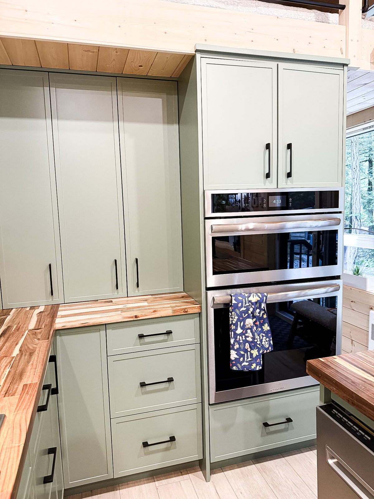 Wall ovens and floor-to-ceiling olive green cabinetry in a modular cabin kitchen