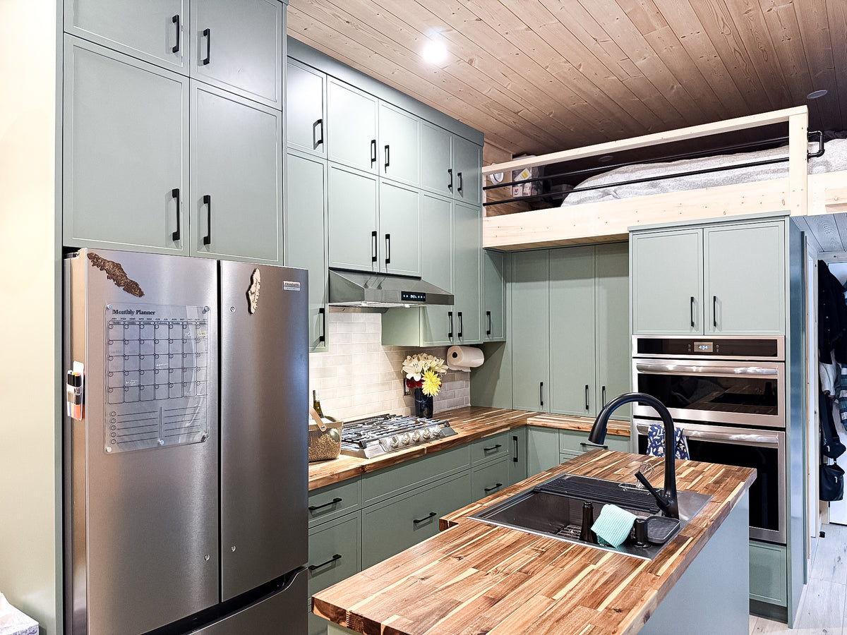 Full kitchen in a modular cabin with floor-to-ceiling olive cabinetry, island, and loft