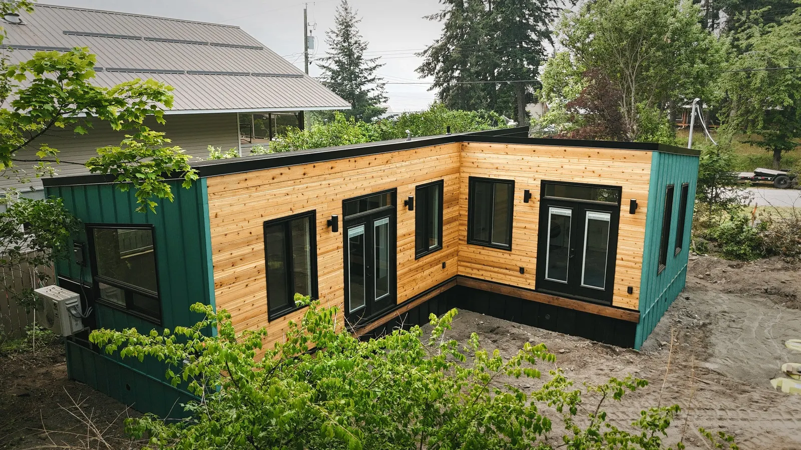 Finished L-shaped modular home in teal metal siding with cedar on the front, two streets from the lake in Silverton, BC